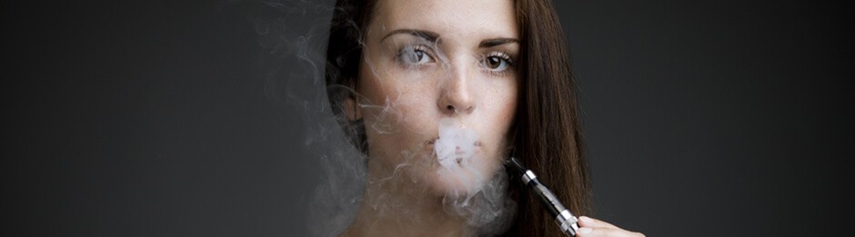 female is looking directly at the camera while exhaling vapor and holding a vape pen in one hand