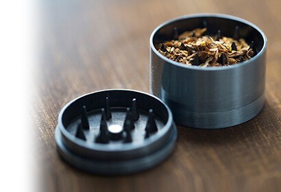 A dry herb grinder on a wooden table with shredded herbs inside