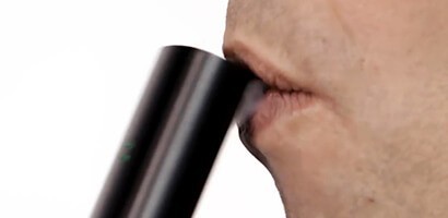Profile of a male taking a drag from pax vaporizer with vapor showing