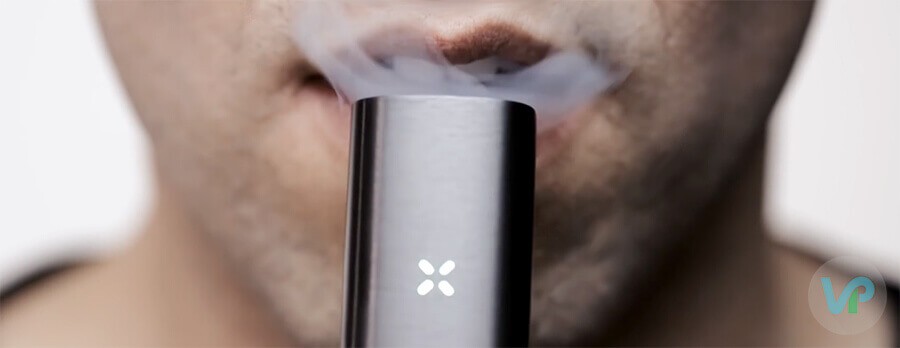 A male taking a drag from Pax vaporizer while smoke is showing